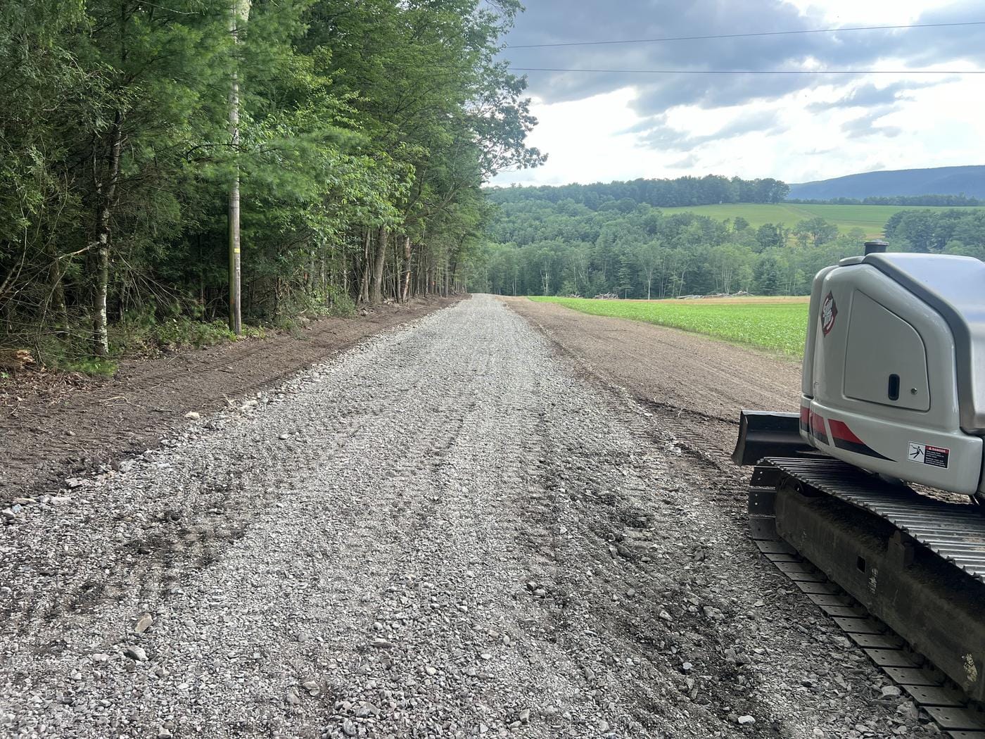 A new stone road along the woods, with the excavator alongside.