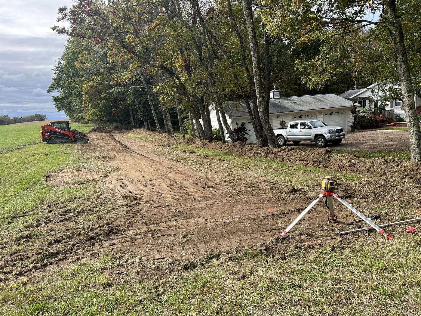 A laser level set up on a fresh strip, with the track loader beyond.
